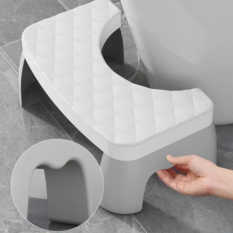 Gray toilet stool with a hand holding it, on a tiled bathroom floor.