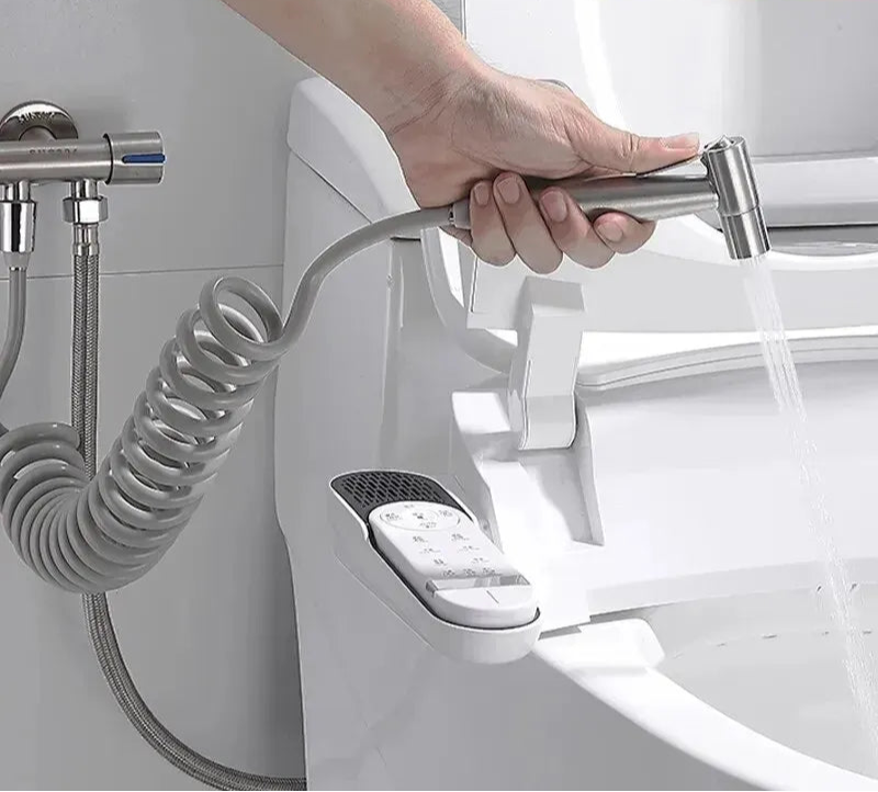 Hand holding a shower head attached to a white bidet with a coiled hose, against a white background.
