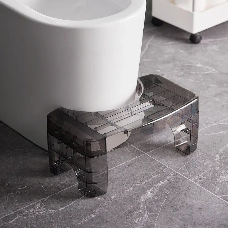 Transparent black step stool in front of a white toilet on a gray tiled floor