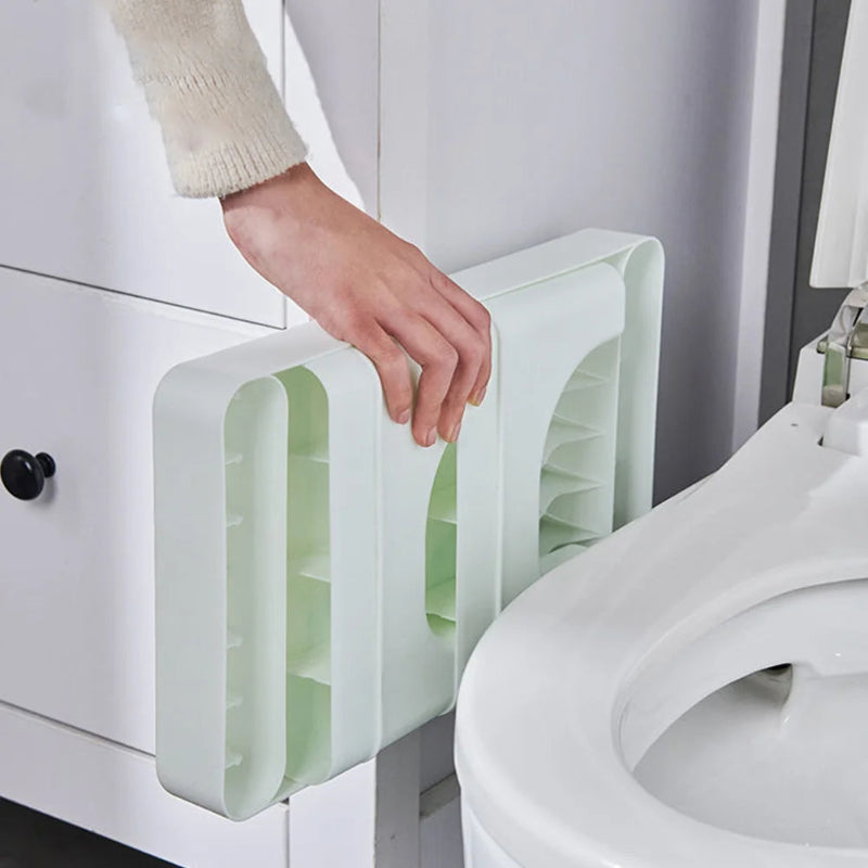 Person using a white and green toilet seat cover holder next to a toilet.